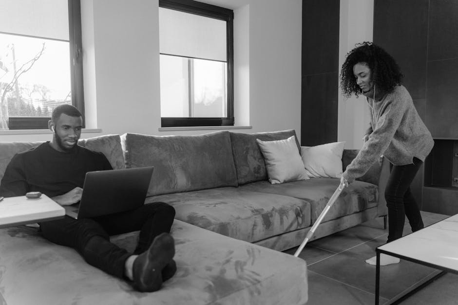 A person using a long-handled duster to clean under a sofa
