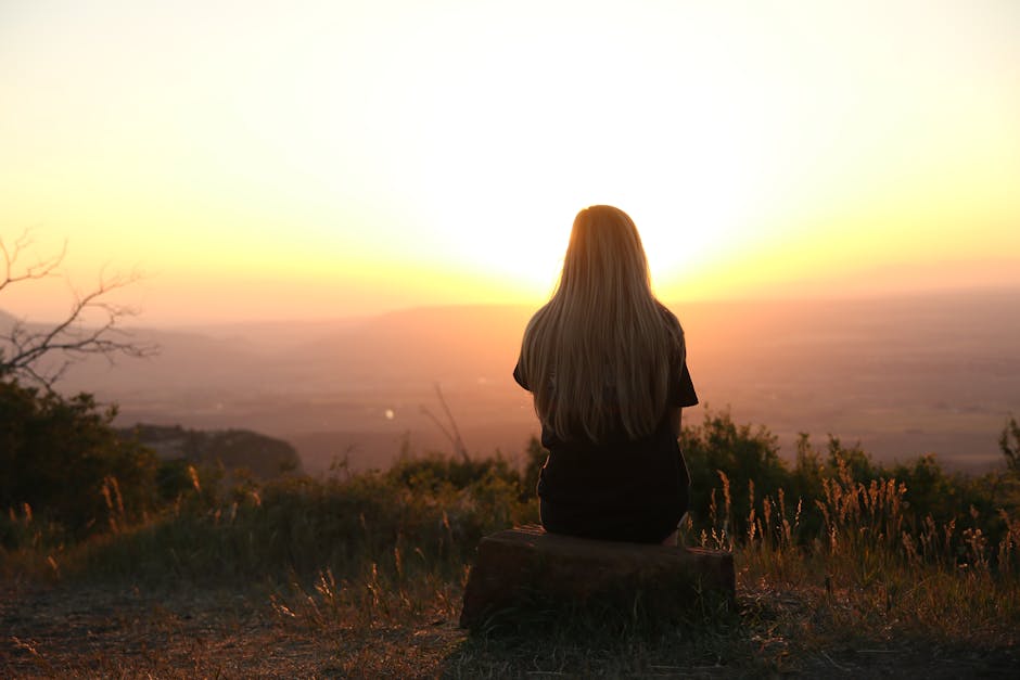 A female student sitting alone on a bench under oak trees, deep in thought as the evening settles