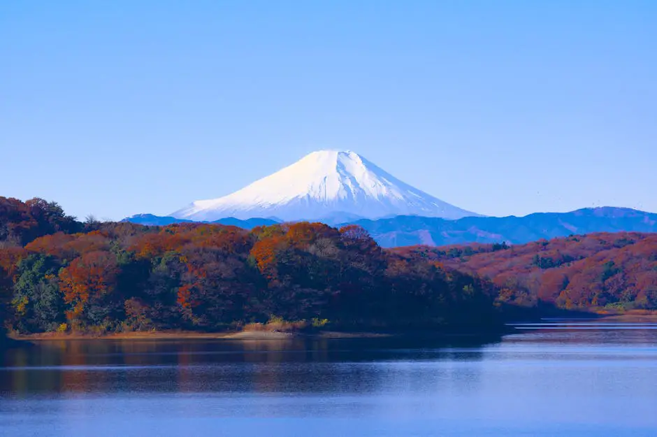 A picturesque autumn landscape in Tasmania, featuring vibrant red and gold foliage surrounding a tranquil lake with mountains in the background
